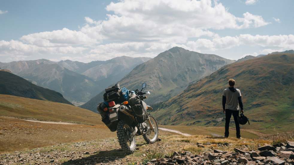 Man stood by motorbike looking at mountain 
